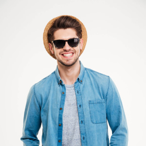 Portrait of cheerful attractive young man in hat and sunglasses over white background